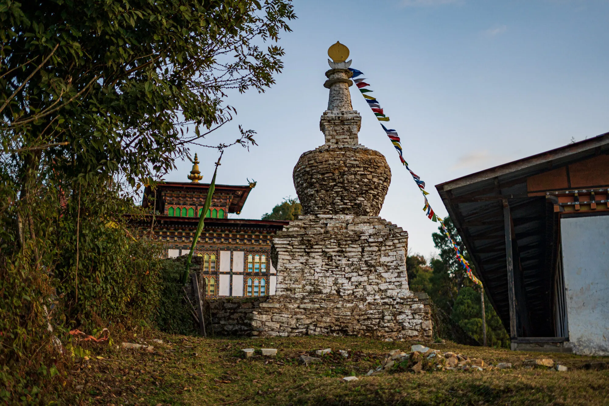 An old whitewashed stone chorten with a gilded top at Dungkhar Goenpa, the main lhakhang’s upper storey and golden finial behind it