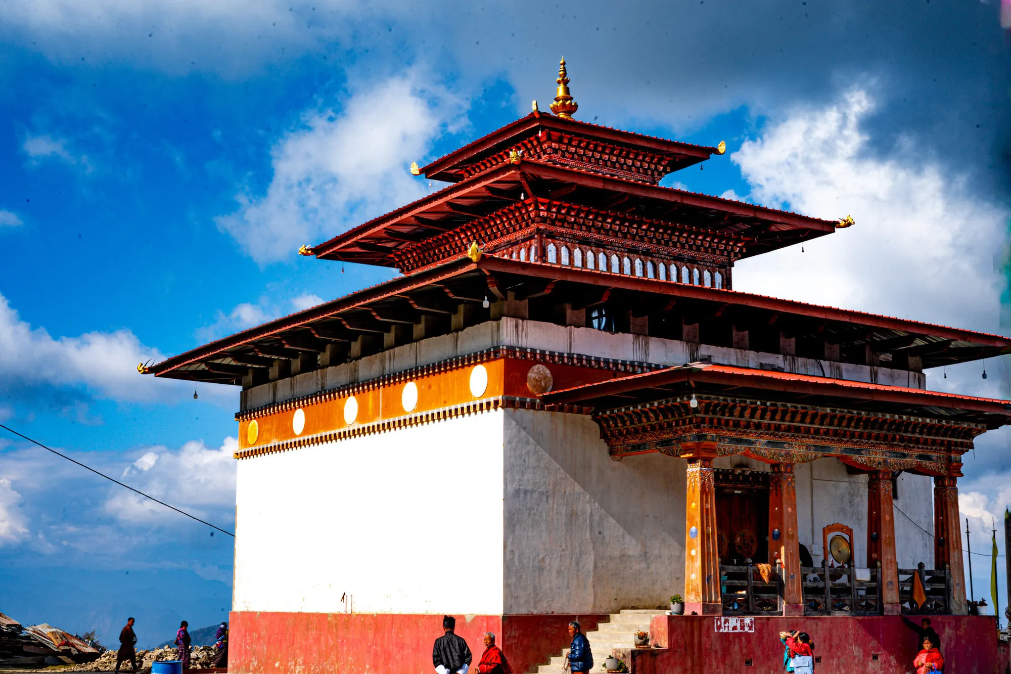 The main lhakhang at Khahor Goenpa: white walls with an orange band, carved porch pillars and a three-tier roof with a golden finial, under a blue sky