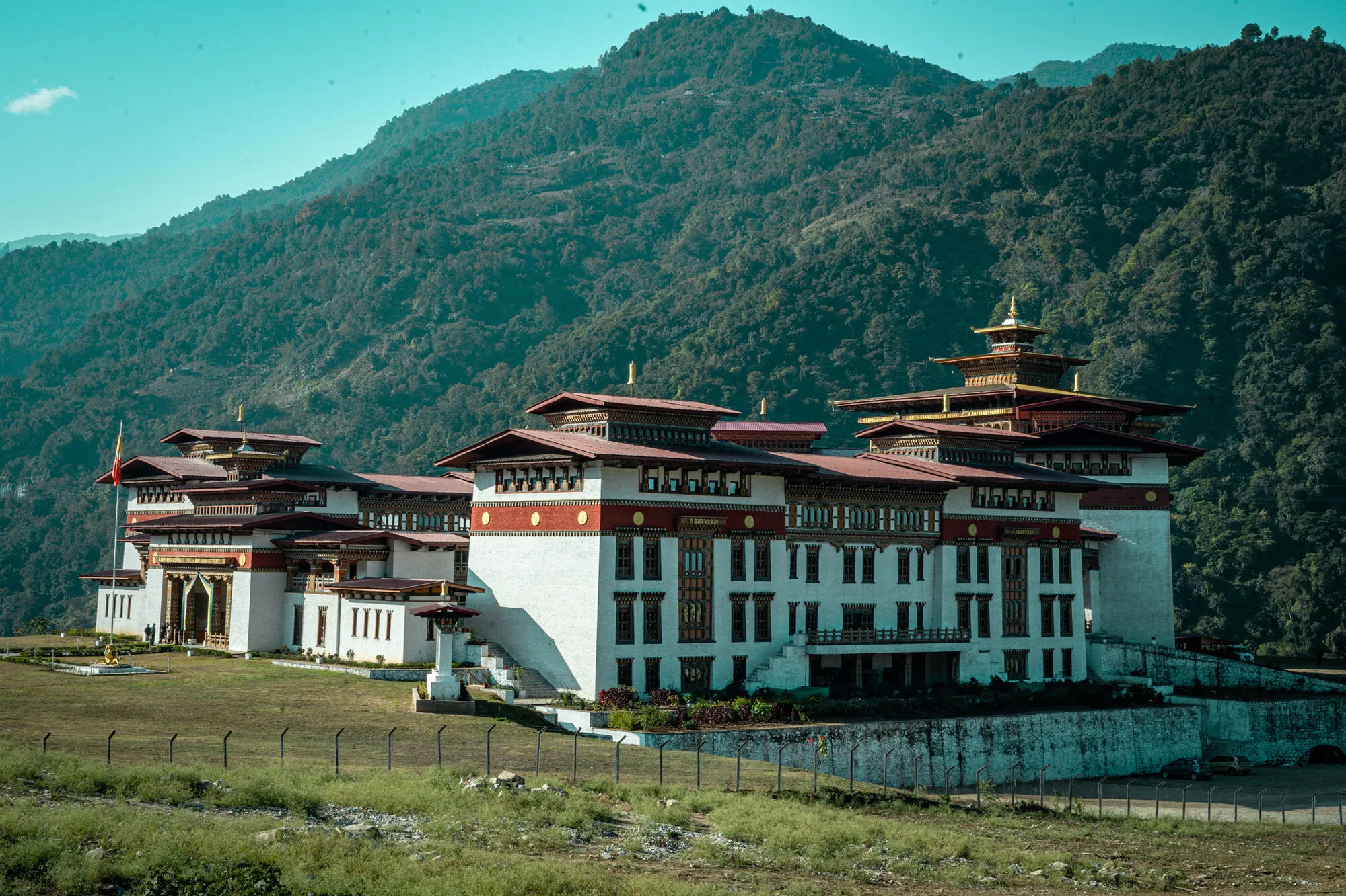 Pemagatshel Dzong at Denchi from the side, standing on grass below a steep forested mountain