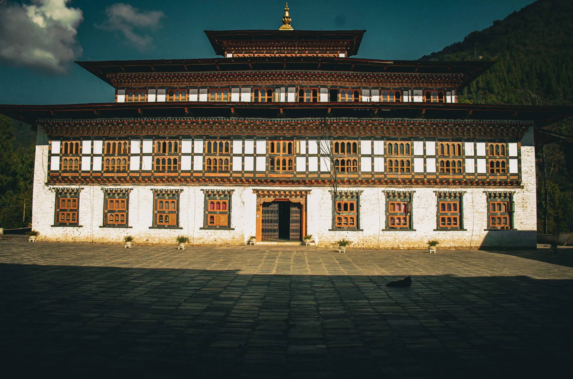 The old Pemagatshel Dzong’s main block across a paved courtyard: a white ground floor, a row of wooden windows above and a raised central roof tier with a gilded pinnacle