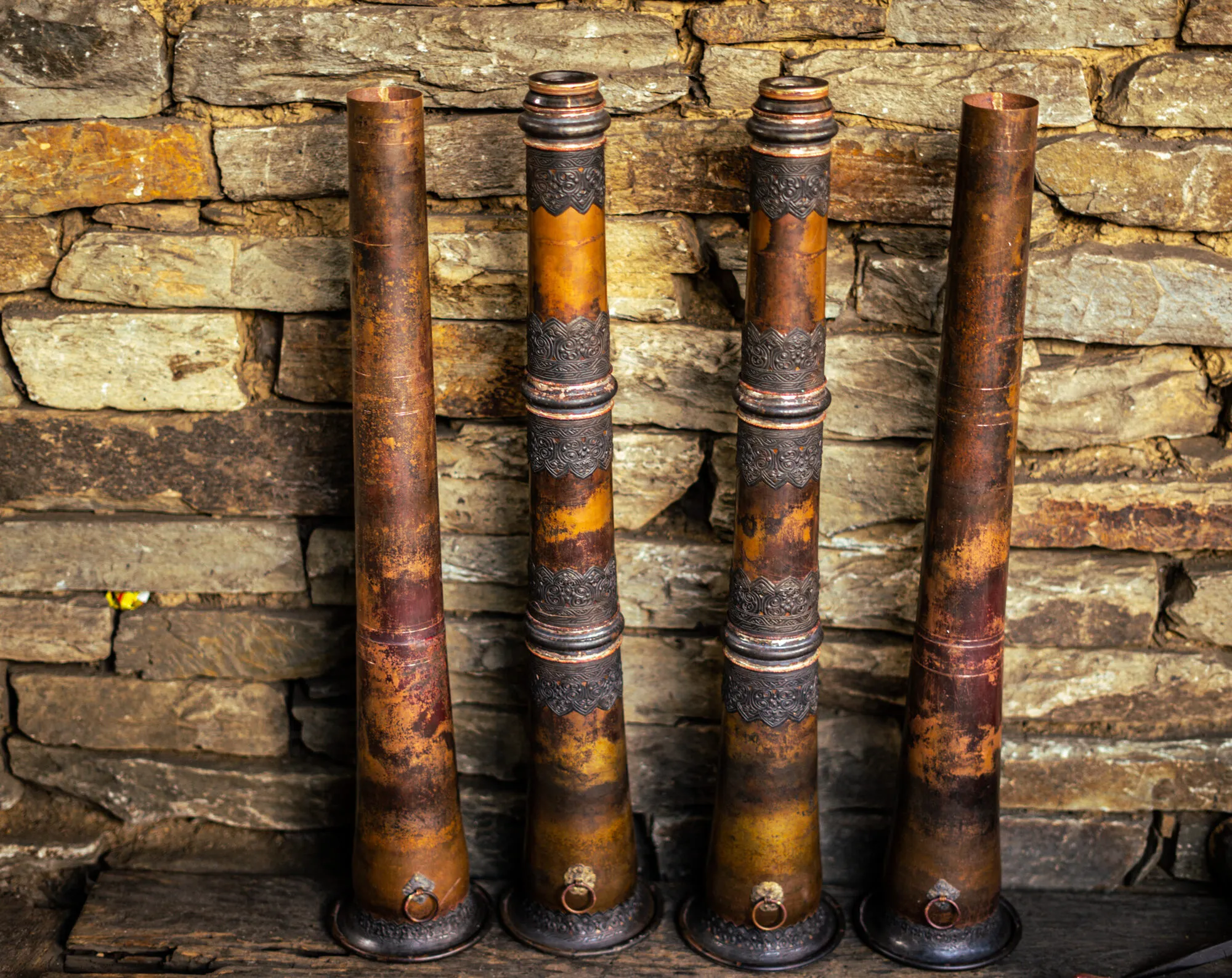 Four horns against a dry-stone wall at Tsebar: two of plain copper, not yet decorated, and two finished with embossed bands