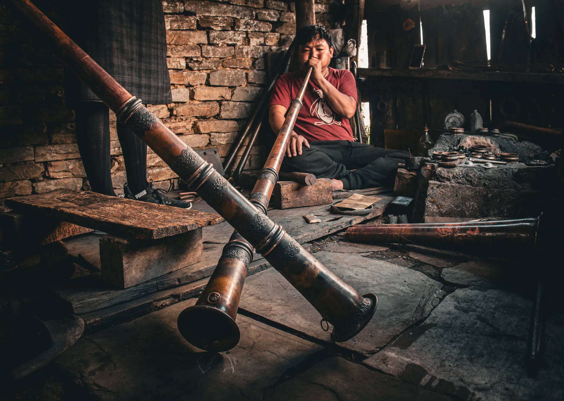A dung maker in his workshop sounding a long horn, a second horn crossing the foreground and the forge bench beside him