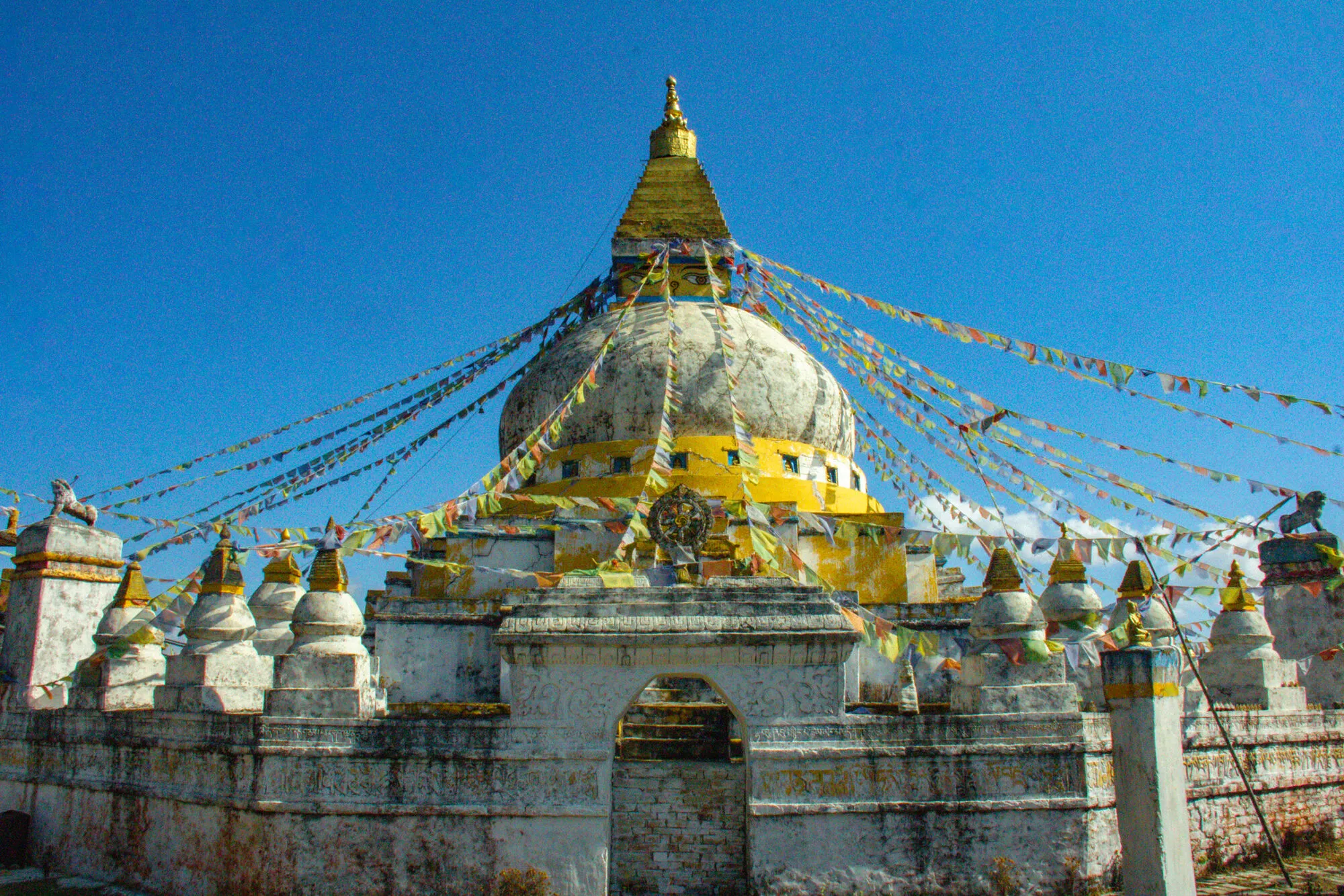 The Tsebar Jarung Khashor Chorten front-on above its whitewashed enclosure, with an arched gateway, a Dharma wheel and stone lions on the corner pillars