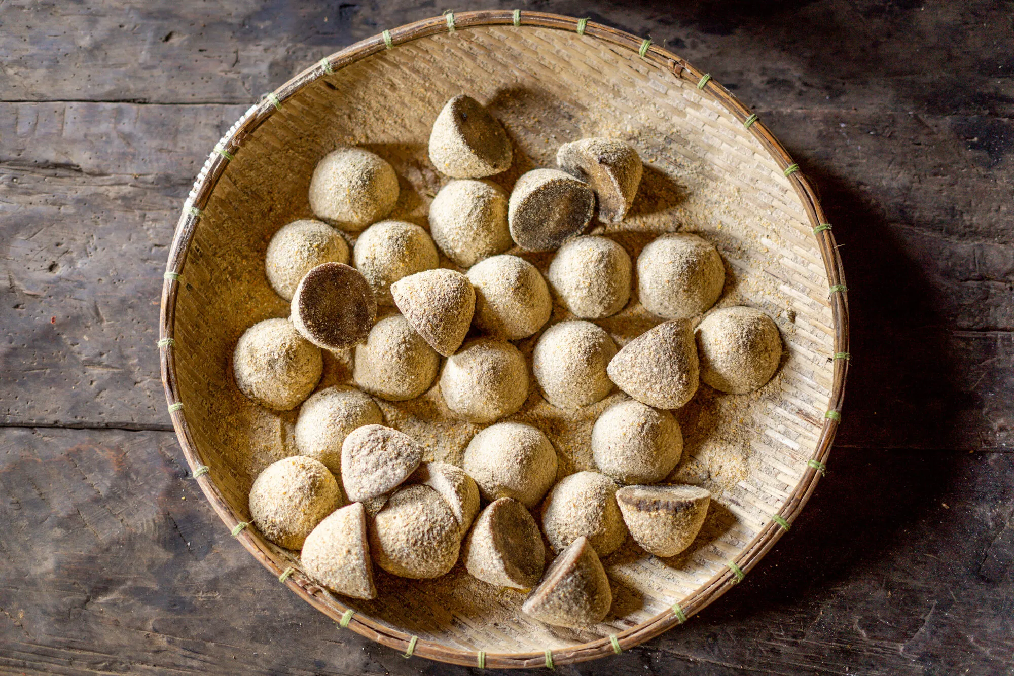 A round bamboo tray of tshatshi buram cones dusted with maize flour, a few turned over to show their dark, flat bases